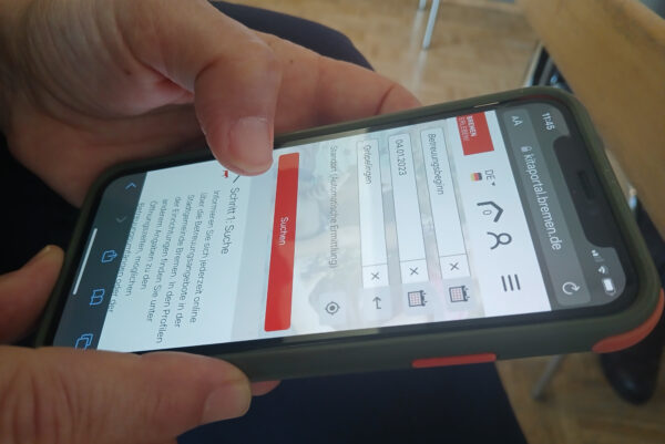 Mit beiden Händen wird ein Handy gehlaten. Zu sehen ist die Startseite des Kita-Portals online.