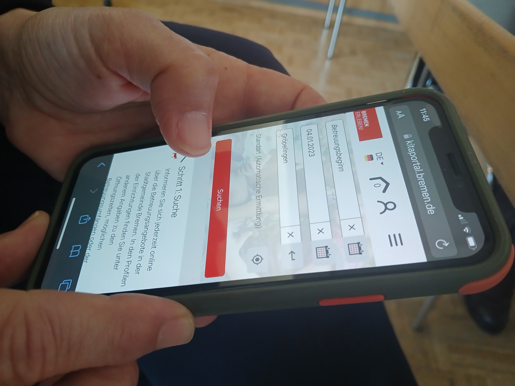 Mit beiden Händen wird ein Handy gehlaten. Zu sehen ist die Startseite des Kita-Portals online.