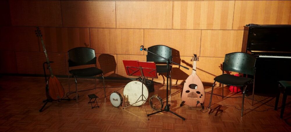 Traditionelle Instrumente wie die Saz und Oud sowie eine Trommel sind für einen Konzertauftritt aufgebaut und werden über einen Spot angestrahlt.