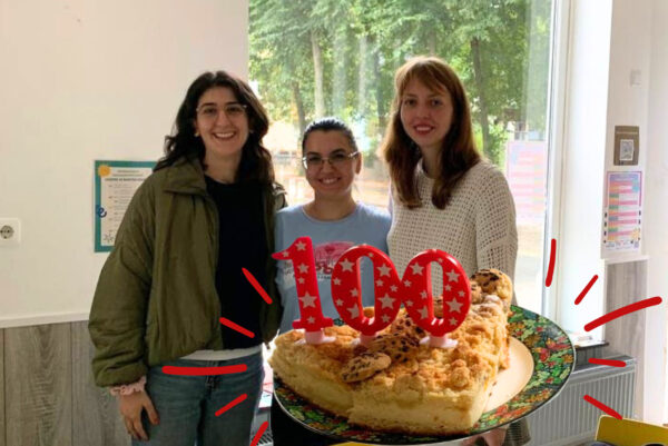 Drei weiblich zu lesende Personen stehen zusammen und lächeln in die Kamera. Direkt unter ihnen ist das Bild von einem Kuchen und der Zahl 100 ins Bild montiert worden.