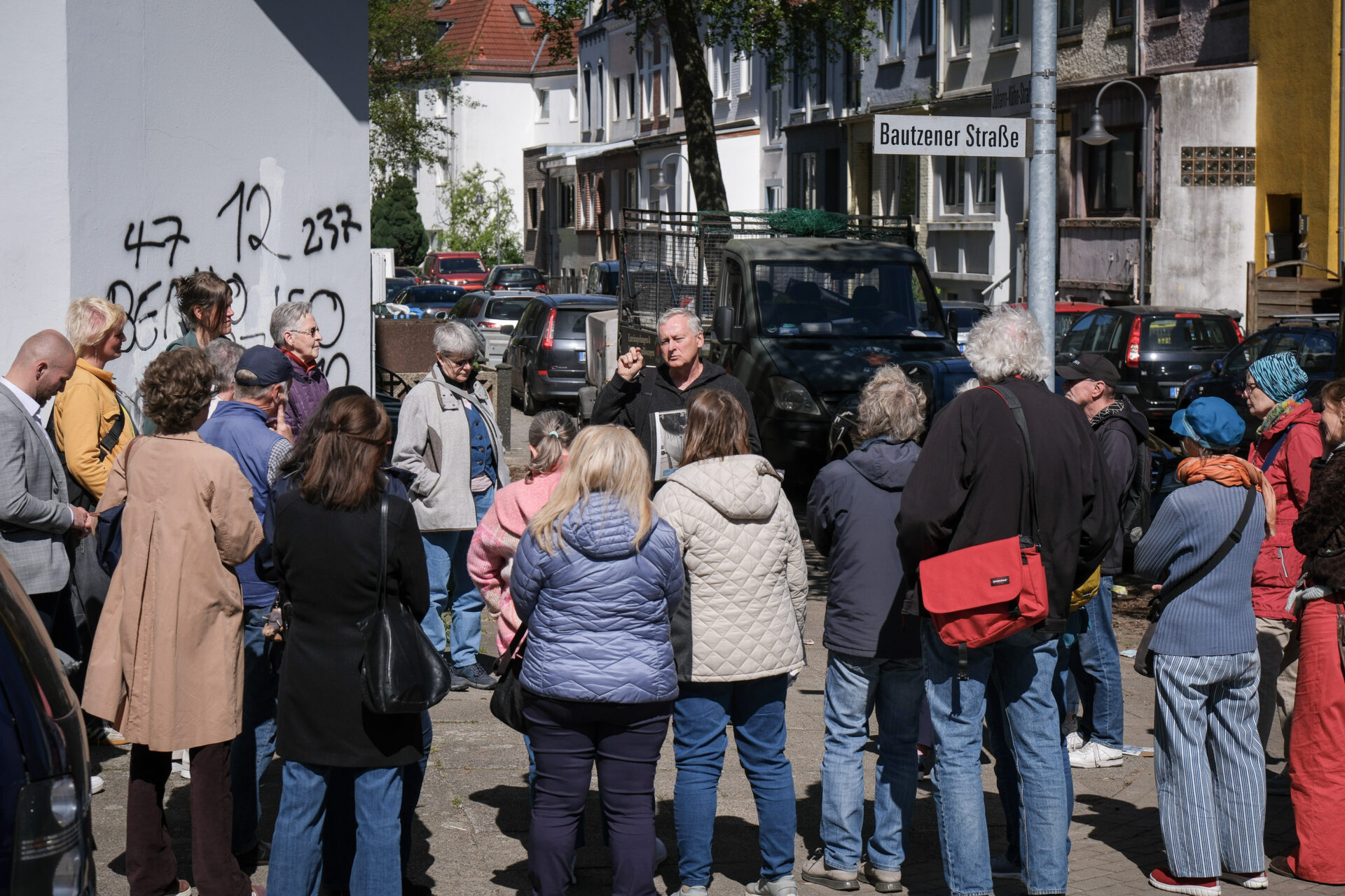Eine Person ist umringt von mehreren anderen an einer Straßenecke. Die Person gestikuliert und spricht.