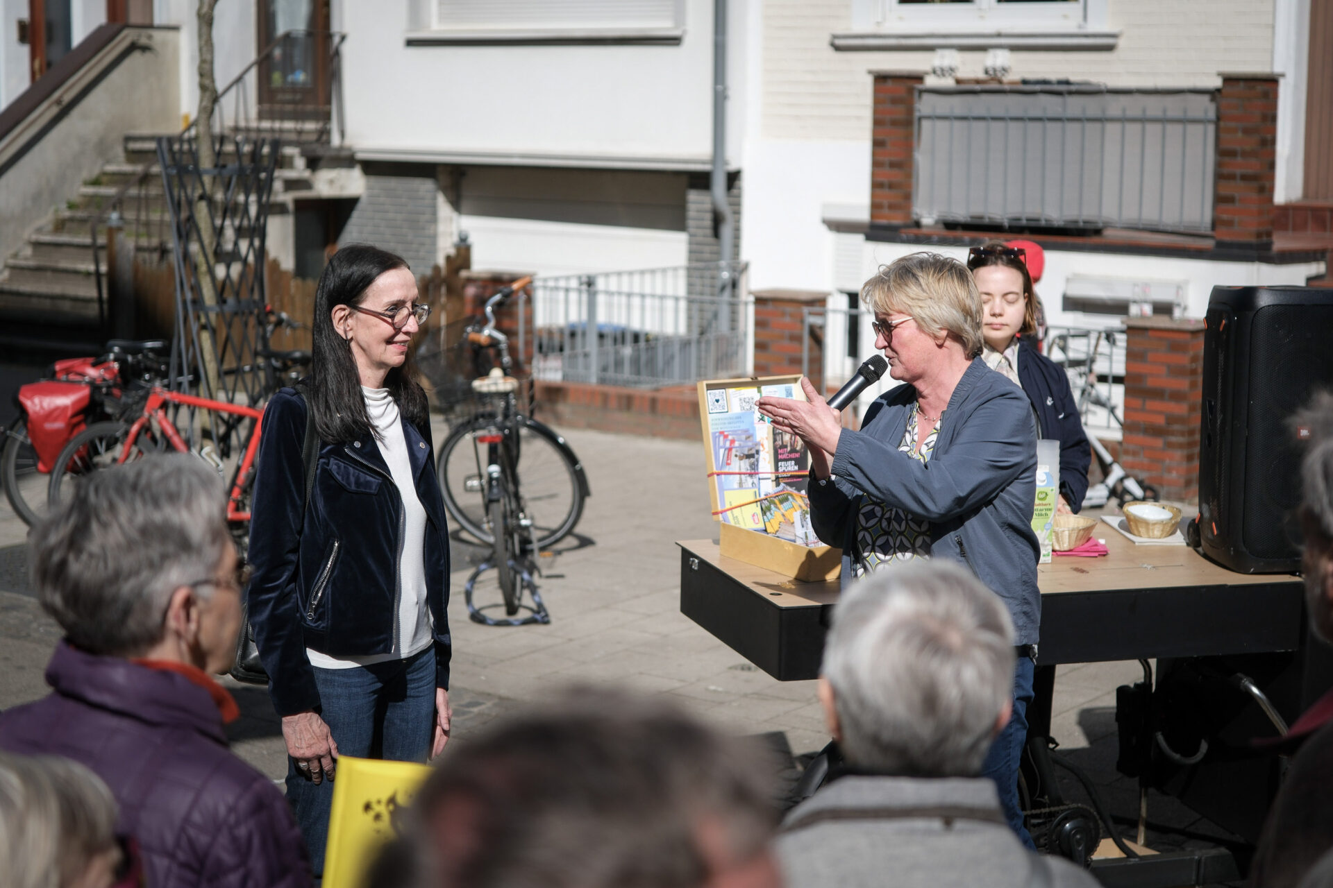 Eine Person hält ein Mikrofon und spricht gestikulierend vor Publikum.