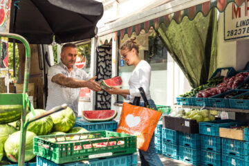 Der Gemüseändler reicht der Kundin ein Stück Melone