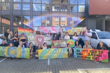 Volontäre aus verschiedenen Ländern erstellen Friedensbanner bei einer Fortbildung im Kinder- und Jugendateier Roter Hahn her. Auf dem Foto zeigen sie in einem Gruppenbild die mehrsprachigen Banner