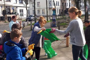 Ein paar Kinder und Erwachsene versammeln sich auf der Straße. Sie teilen Müllsäcke und Handschuhe zum Müllsammeln aus.