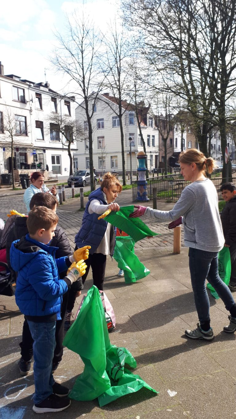 Ein paar Kinder und Erwachsene versammeln sich auf der Straße. Sie teilen Müllsäcke und Handschuhe zum Müllsammeln aus.