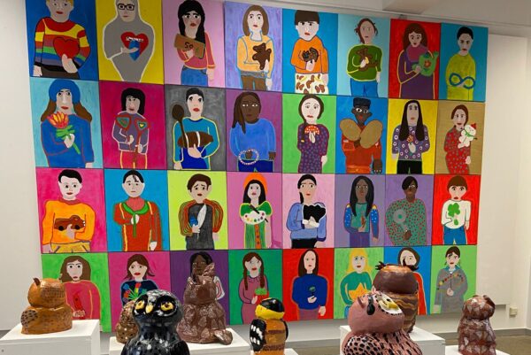 In einem Raum sind gemalte Portraits und Eulen aus Ton zu sehen.