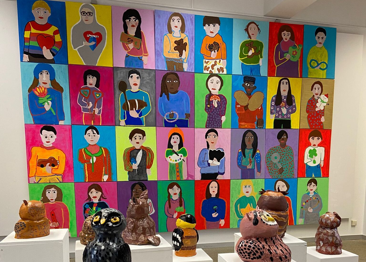 In einem Raum sind gemalte Portraits und Eulen aus Ton zu sehen.