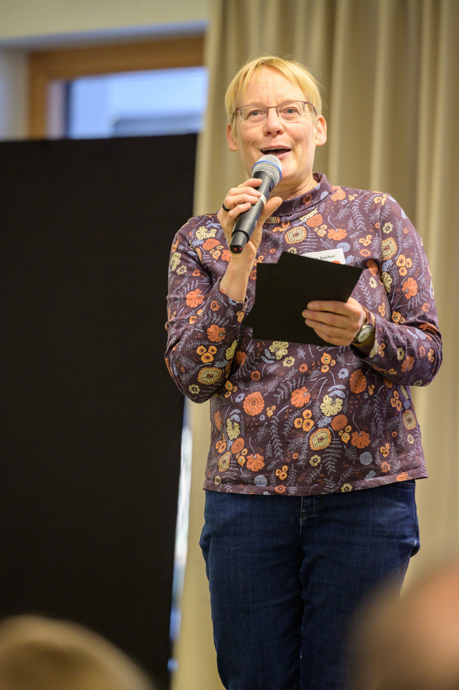 Eine Person mit blumigen Oberteil spricht über ein Mikrofon.