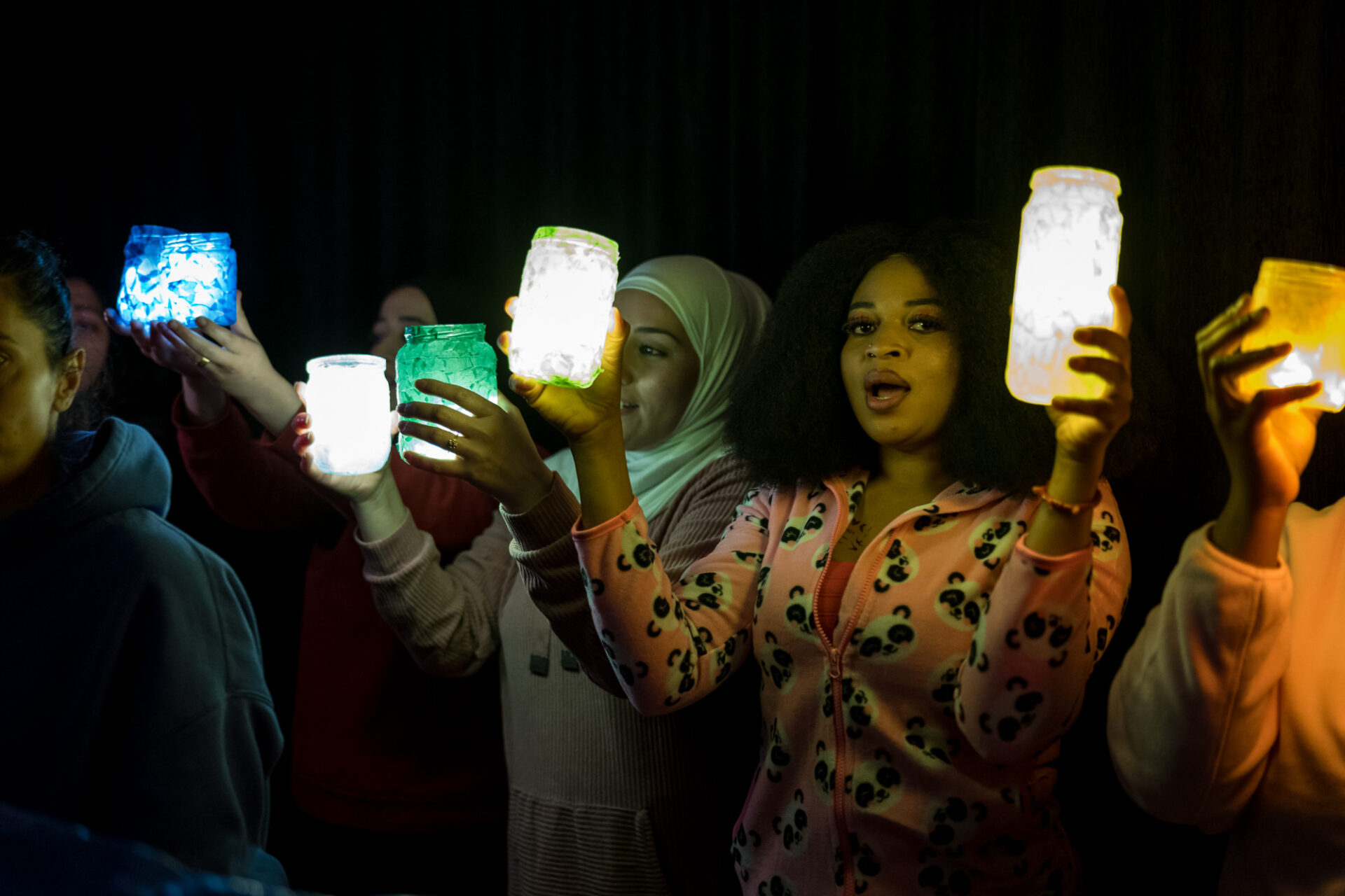 In der Dunkelheit halten mehrere Personen große Teelichter hoch und singen.