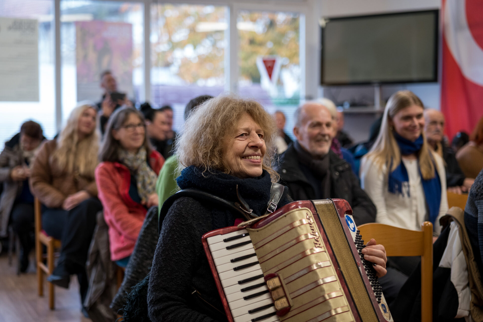 Ein lächelndes Publikum  sitzt in Stuhlreihen.
