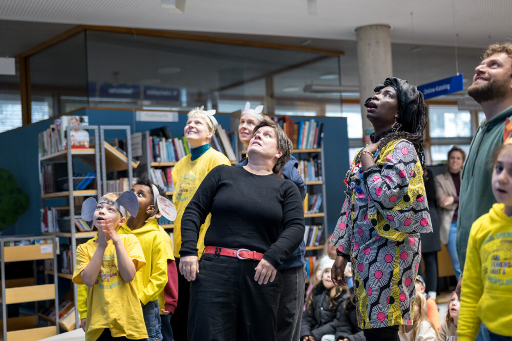 Mehrere bunt gekleidete Personen unterschiedlichen Alters schauen ausdrucksstark nach oben.