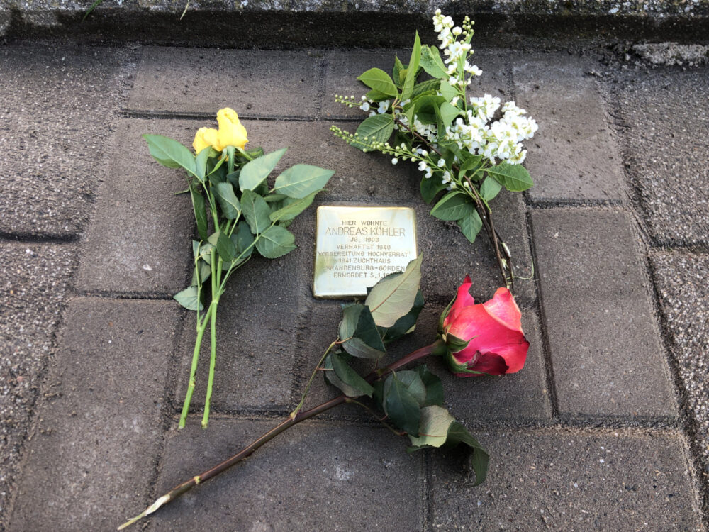 Ein Stolperstein, umrahmt von Blumen