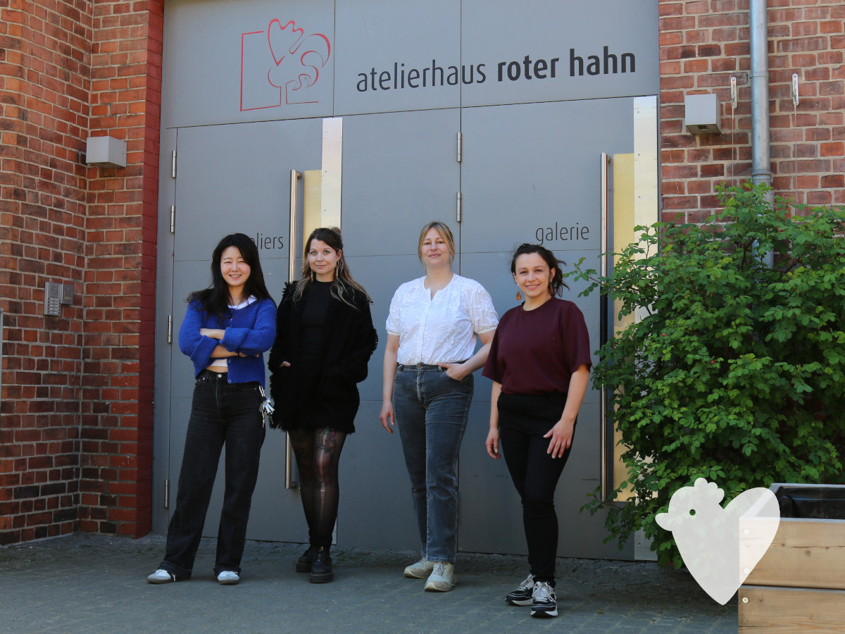 Vier Frauen stehen selbstbewußt vor einer großen Haustür an der steht: atelierhaus roter hahn"