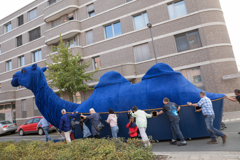 Einige Menschen schieben ein circa 12 Meter großes blaues Lama auf der Straße. 
