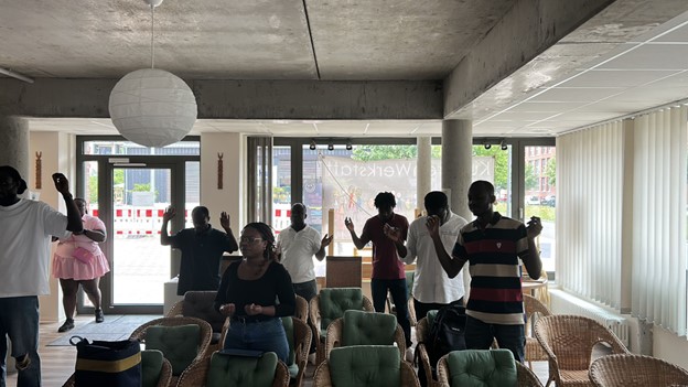 Singende Menschen stehen in einem Raum, in dem einige Stühle vor einen Gottesdienst aufgestellt sind. 