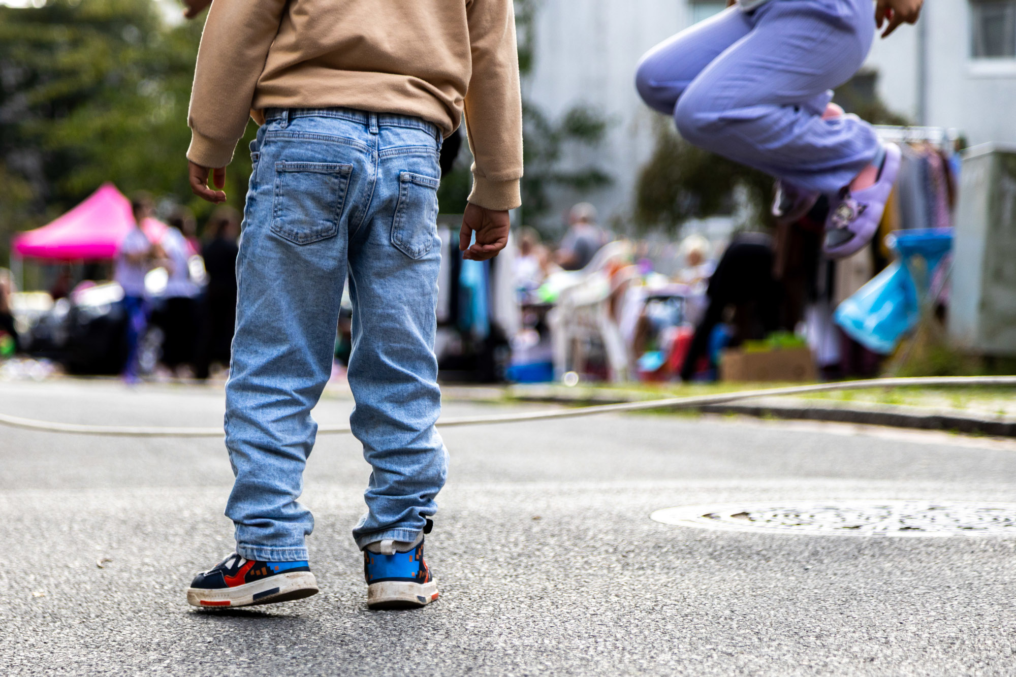 Mitten auf einer Staße sind Kinderbeine zu sehen. Eins der Kinder hüpft in die Luft.