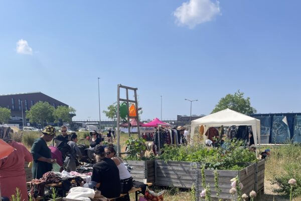 Flohmarktsituation auf einer offenen Fläche mit Hochbeeten mit Blumen, Verkaufsständen und Pavillons.