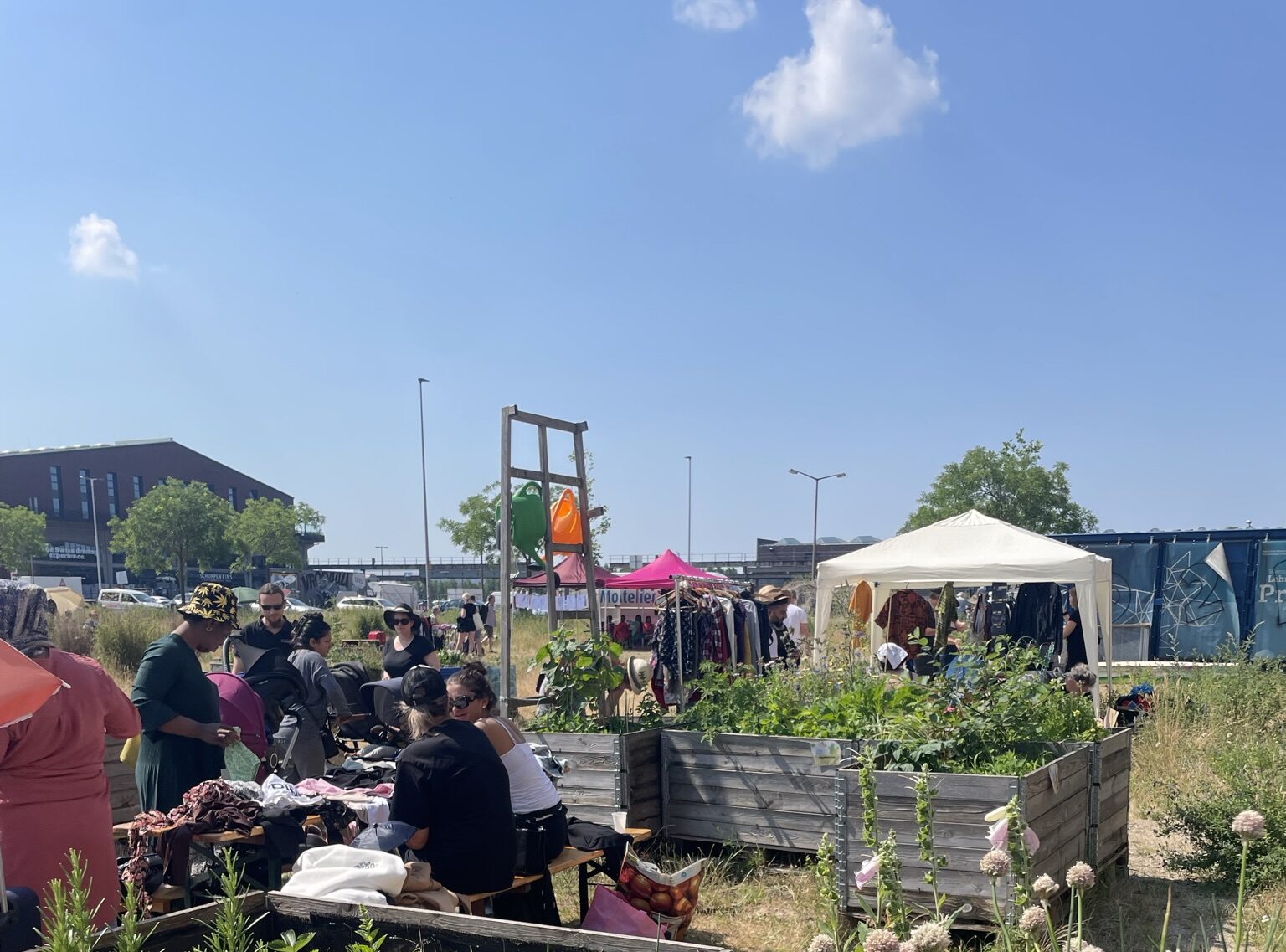 Flohmarktsituation auf einer offenen Fläche mit Hochbeeten mit Blumen, Verkaufsständen und Pavillons.