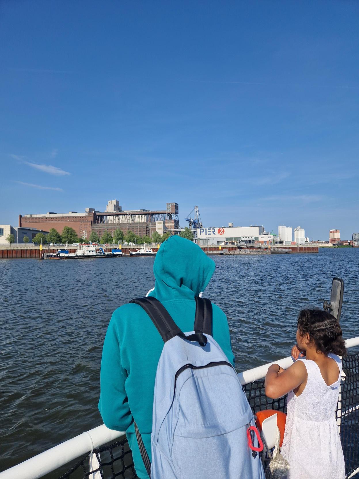 An de rReling eines Schiffes stehen zwei Personen und schauen aufs Wasser.