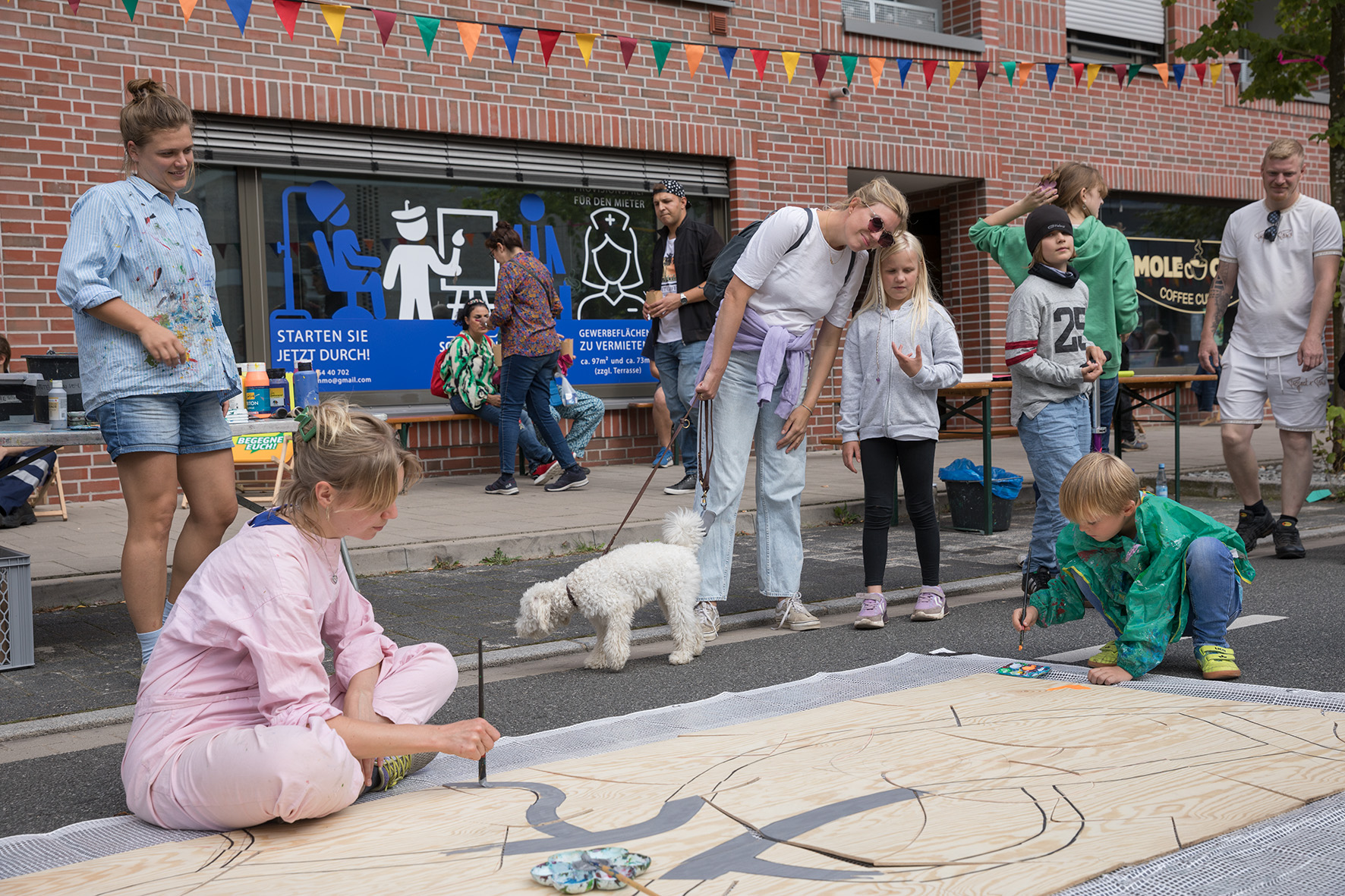 Auf der Straße bemalen Kinder und Erwachsene eine große Holzplatte.