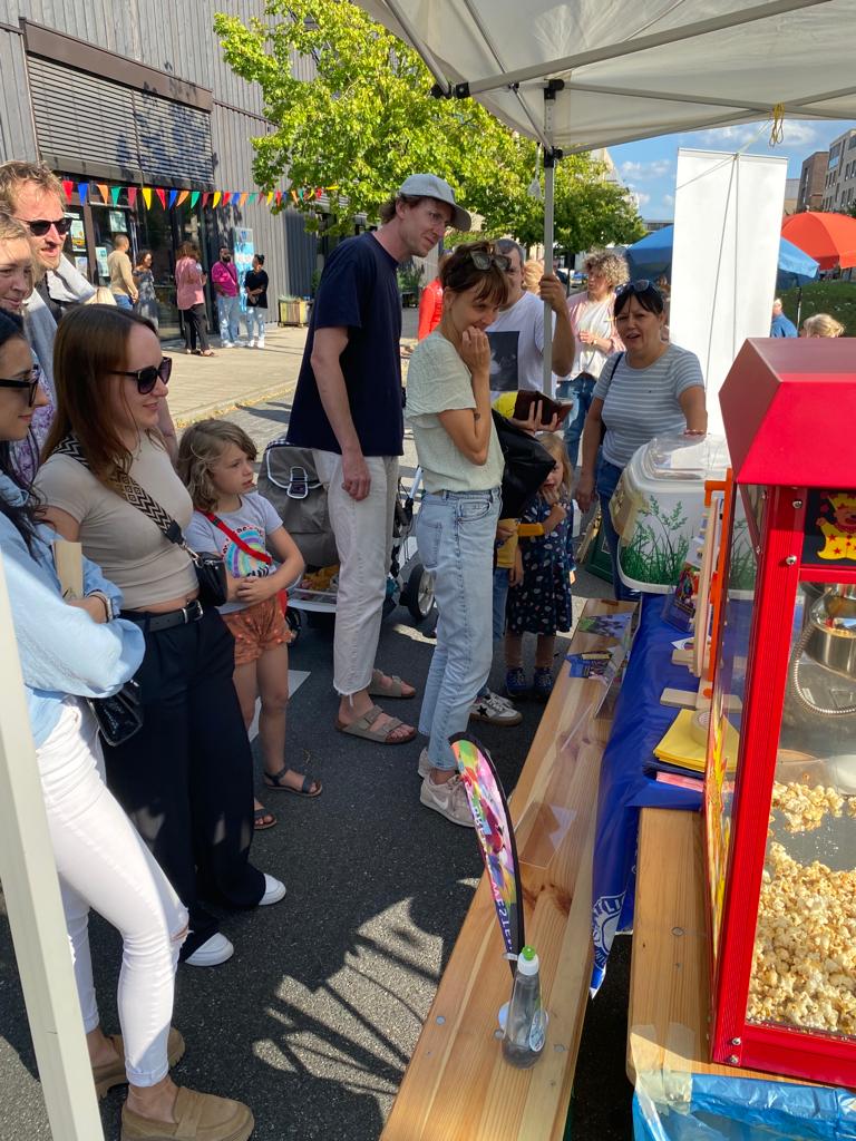 Eine Popcorn Maschine steht auf einem Tisch. Kinder und Erwachsene schauen neugierig, was es an diesem Tisch zu entdecken gibt.