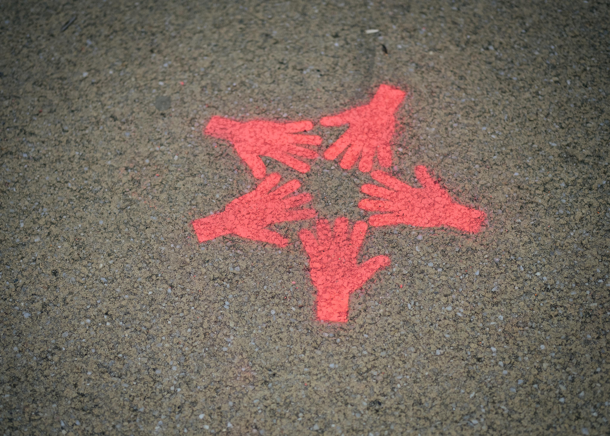 Auf einen Asphaltboden sind fünf sich berührende Hände mit Sprühkreide aufgesprüht