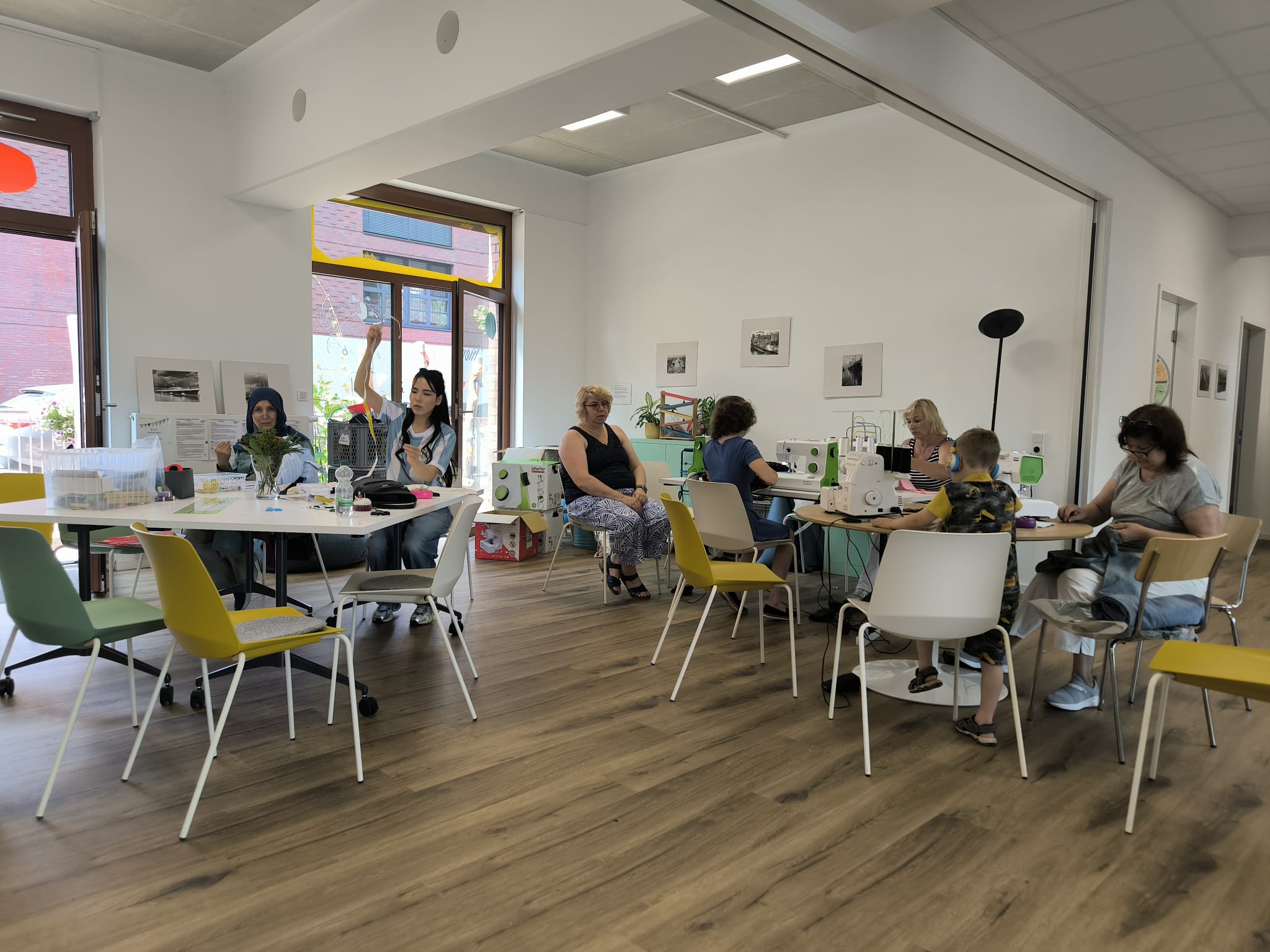 Es sind sieben Personen im Quartierstreff Jetzt Hier zu sehen. Sie alle sind beschäftigt mit Nähen, Stoffe schneiden oder ähnlichem.