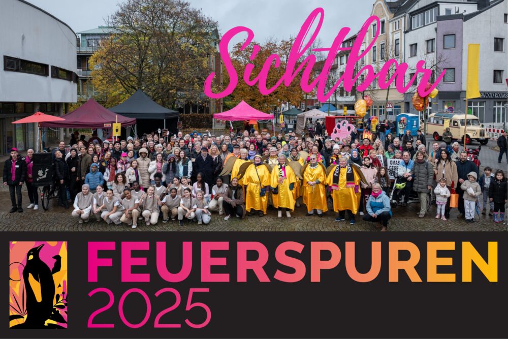 Auf dem Gröpelinger Bibliotheksplatz haben sich alle Beteiligten des Festival Feuerspuren versammelt zu einem Gruppenfoto. Manche sind kostümiert. Der Schriftzug "Sichtbar" und das Feuerspuren Logo wurde eingebaut.