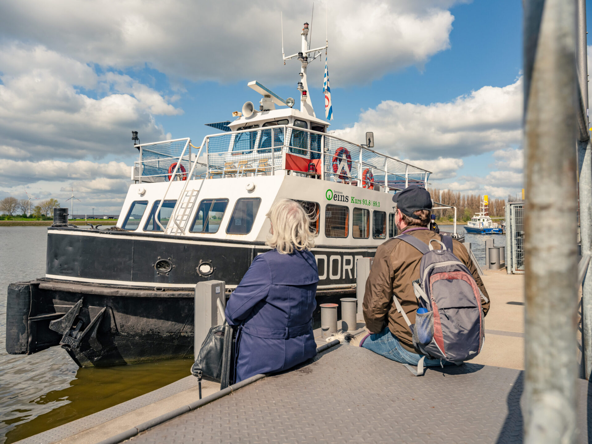Das ist der Schiffsanleger Pier 2 / Waterfont. Zwei Personen sehen zu, wie die Weserfähre Bremen am Anleger anlegt. Ein kleiner Hund ist auch auf dem Anleger.