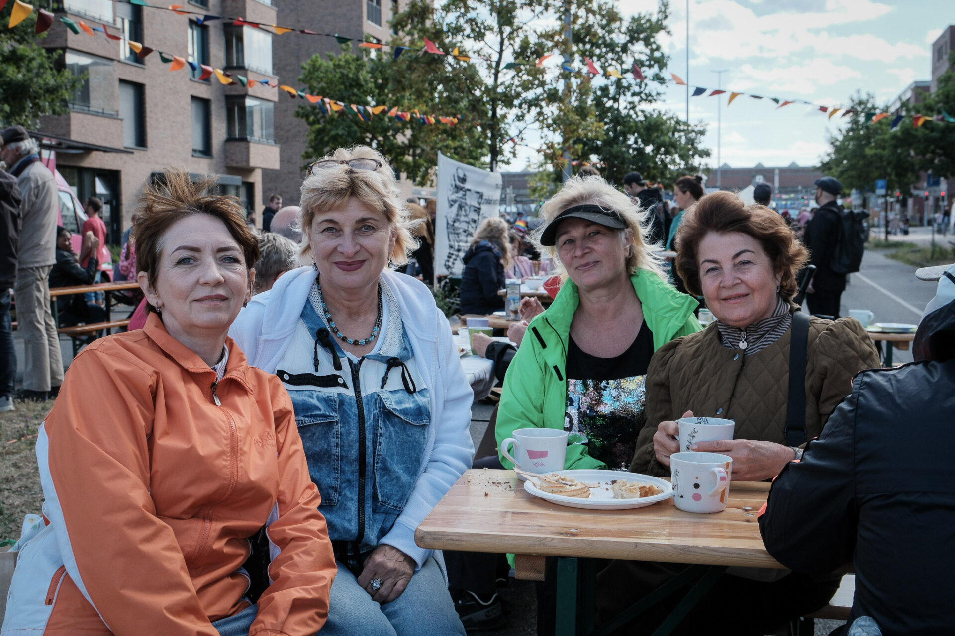 Vier Frauen sitzen beim Kaffee trinken zusammen und lachen in die Kamera.