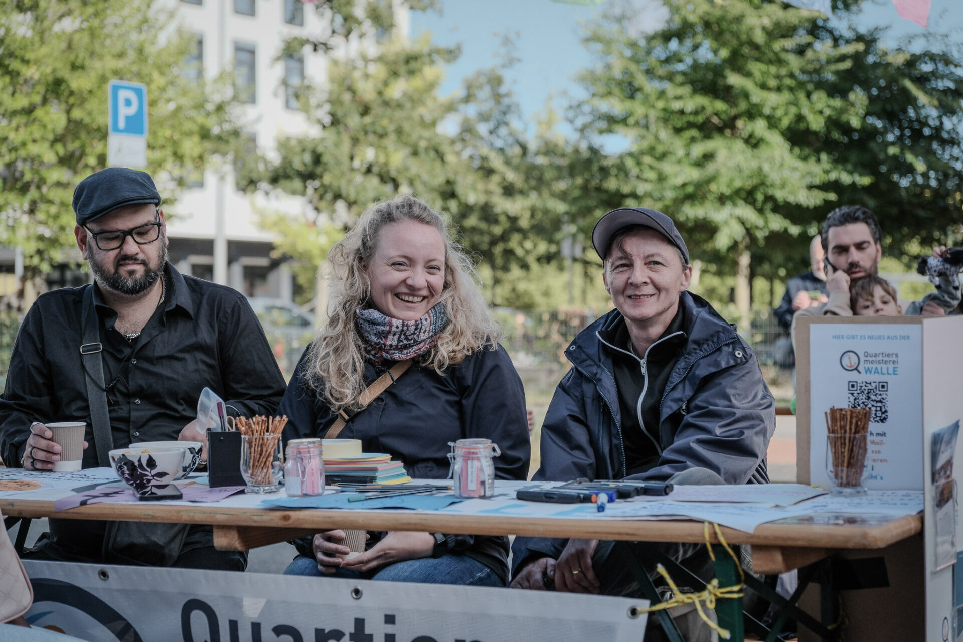 Evin und Janine von der Quartiersmeisterei Walle lachen in die Kamera. Ein weiterer Mann sitzt mit auf der Bank.