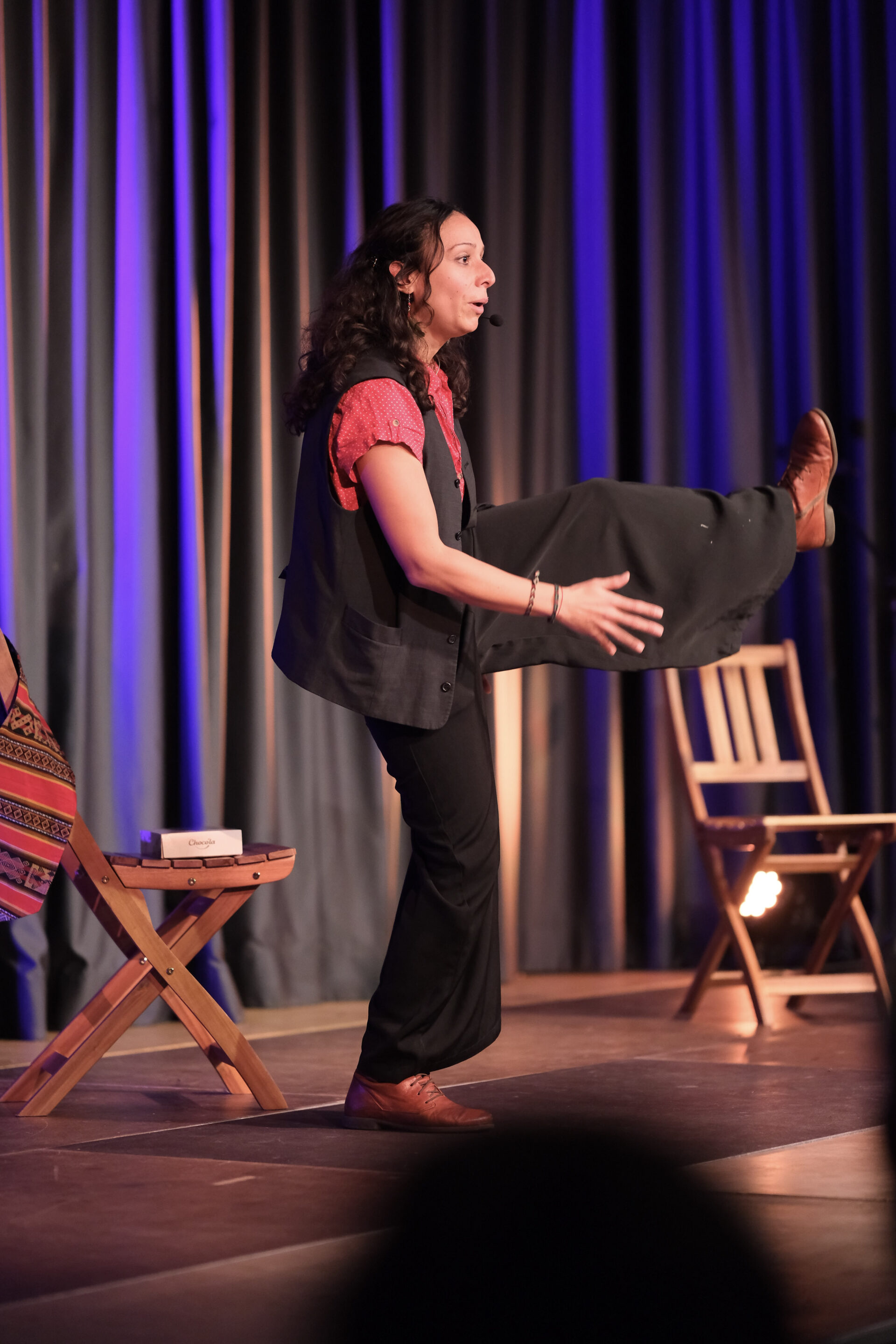 Auf einer Bühne steht eine Person in der Bewegung erstarrt auf einem Bein. 