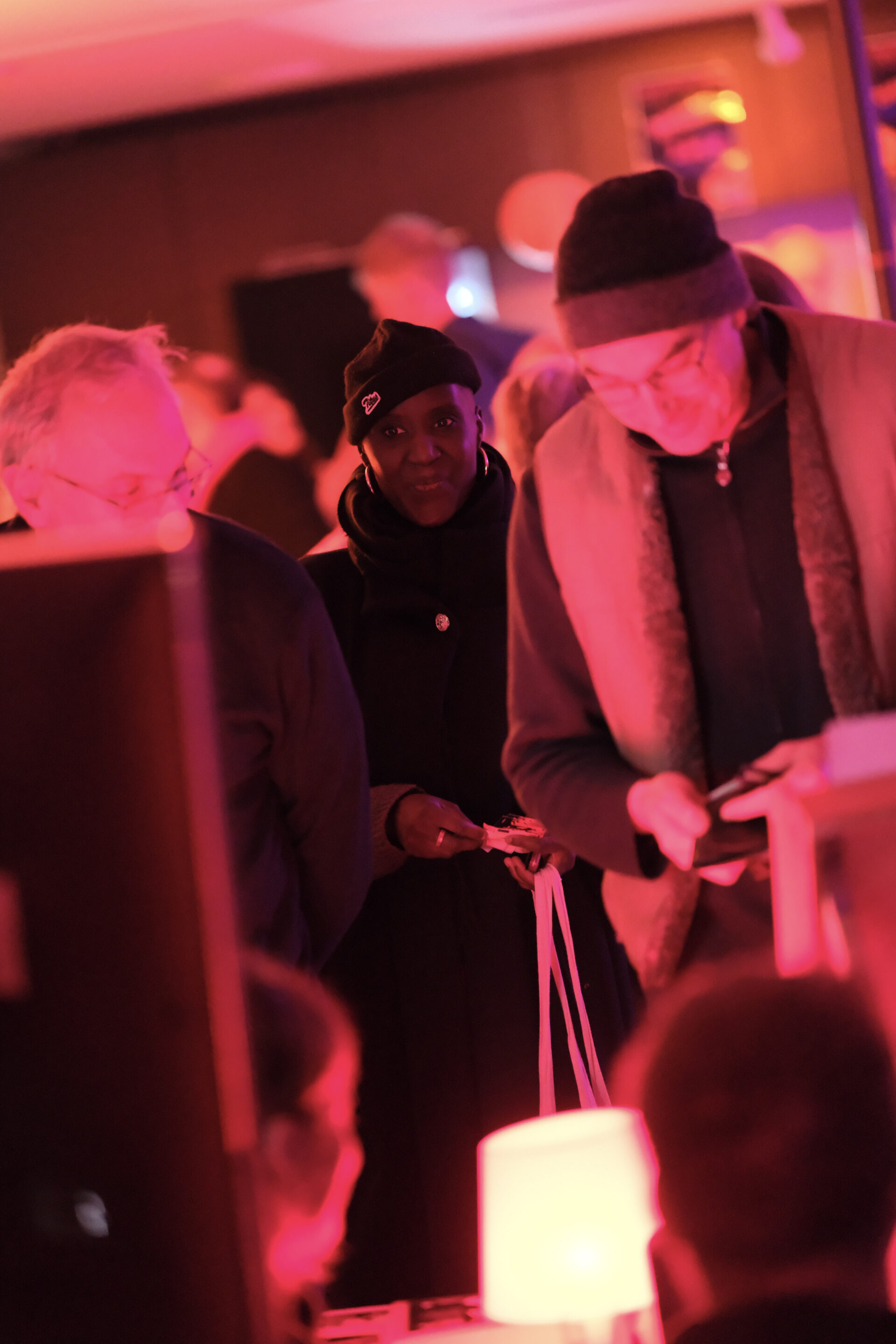 In einem rot beleuchteten Raum stehen mehrere Personen über einen Stand gebeugt. Eine Person schaut direkt in die Kamera.