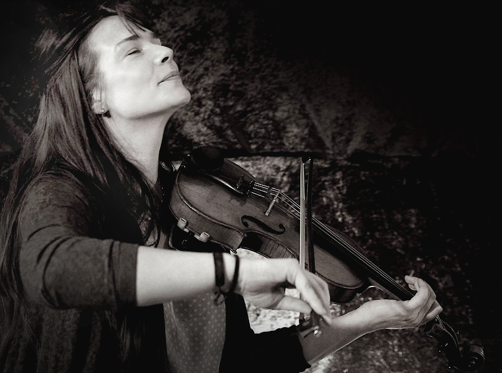 Eine Person spielt eine Geige mit geschlossenen Augen. Der Bogen berührt die Saiten, während das Instrument unter dem Kinn gehalten wird. Das Foto ist in Schwarz-Weiß aufgenommen und zeigt eine konzentrierte, ruhige Szene.
