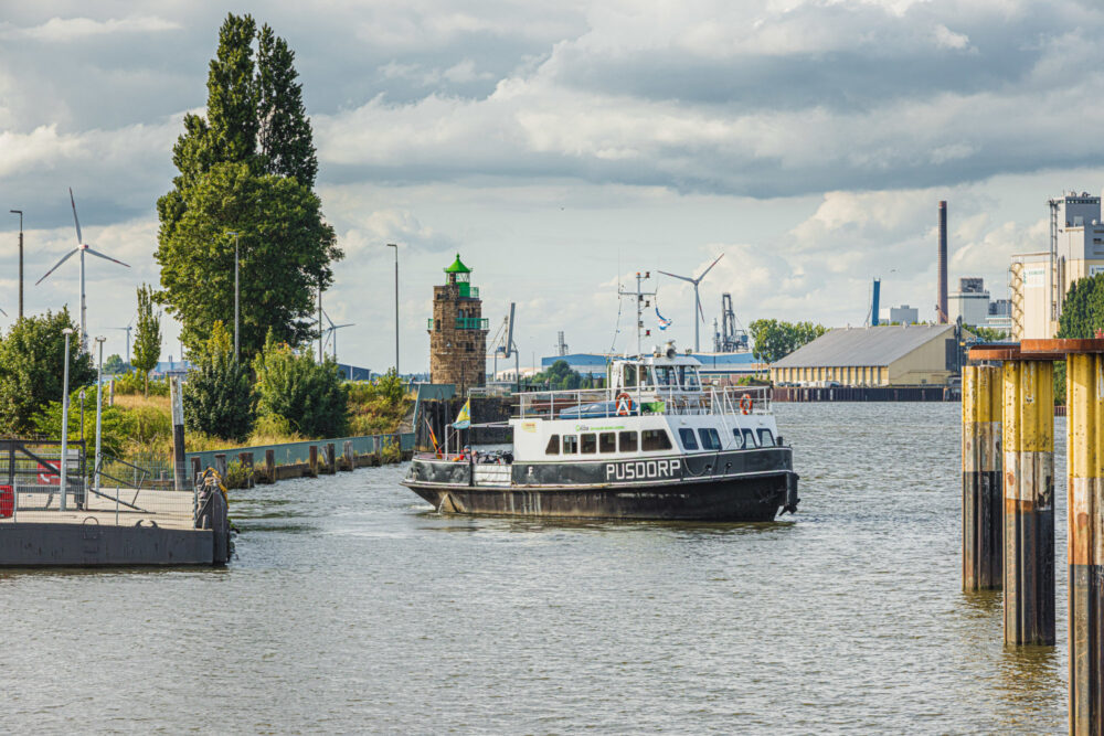 Ein Fährschiff entfernt sich von einem Schiffsanleger und dreht sich auf dem Wasser. Rechts sind Dalben zu sehen.