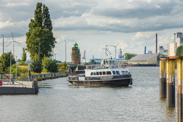 Ein Fährschiff entfernt sich von einem Schiffsanleger und dreht sich auf dem Wasser. Rechts sind Dalben zu sehen.