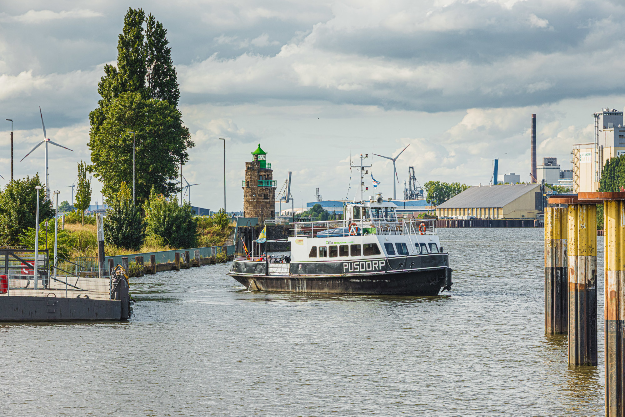 Ein Fährschiff entfernt sich von einem Schiffsanleger und dreht sich auf dem Wasser. Rechts sind Dalben zu sehen.