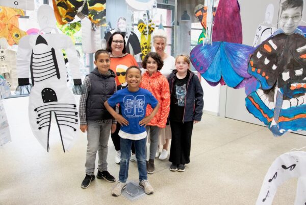 Inmitten einer Ausstellung stehen Erwachsene und Kinder zusammen und schauen in die Kamera.