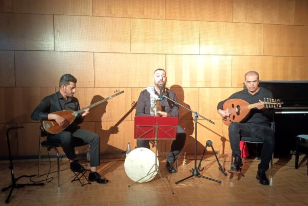 Drei Musiker spielen sitzend auf traditionellen Instrumenten. Der Musiker in der Mitte singt.