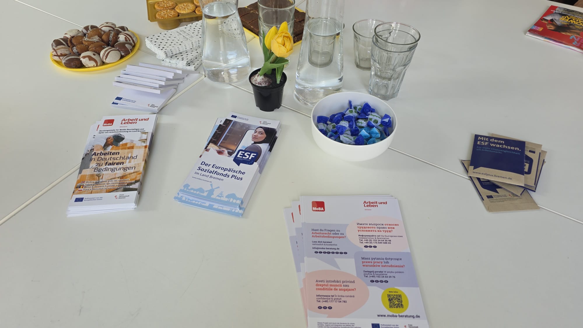 Auf einem weißen Tisch liegen Info-Flyer und Knabbereien