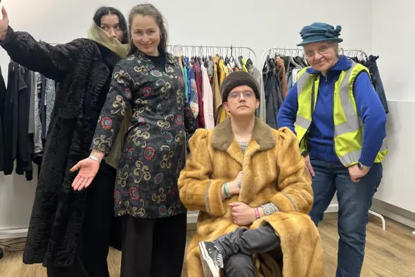 vier Personen posieren in ausgefallener Kleidung für die Kamera. Im hintergrund ist ein Kleiderständer mit vielen Klamotten.