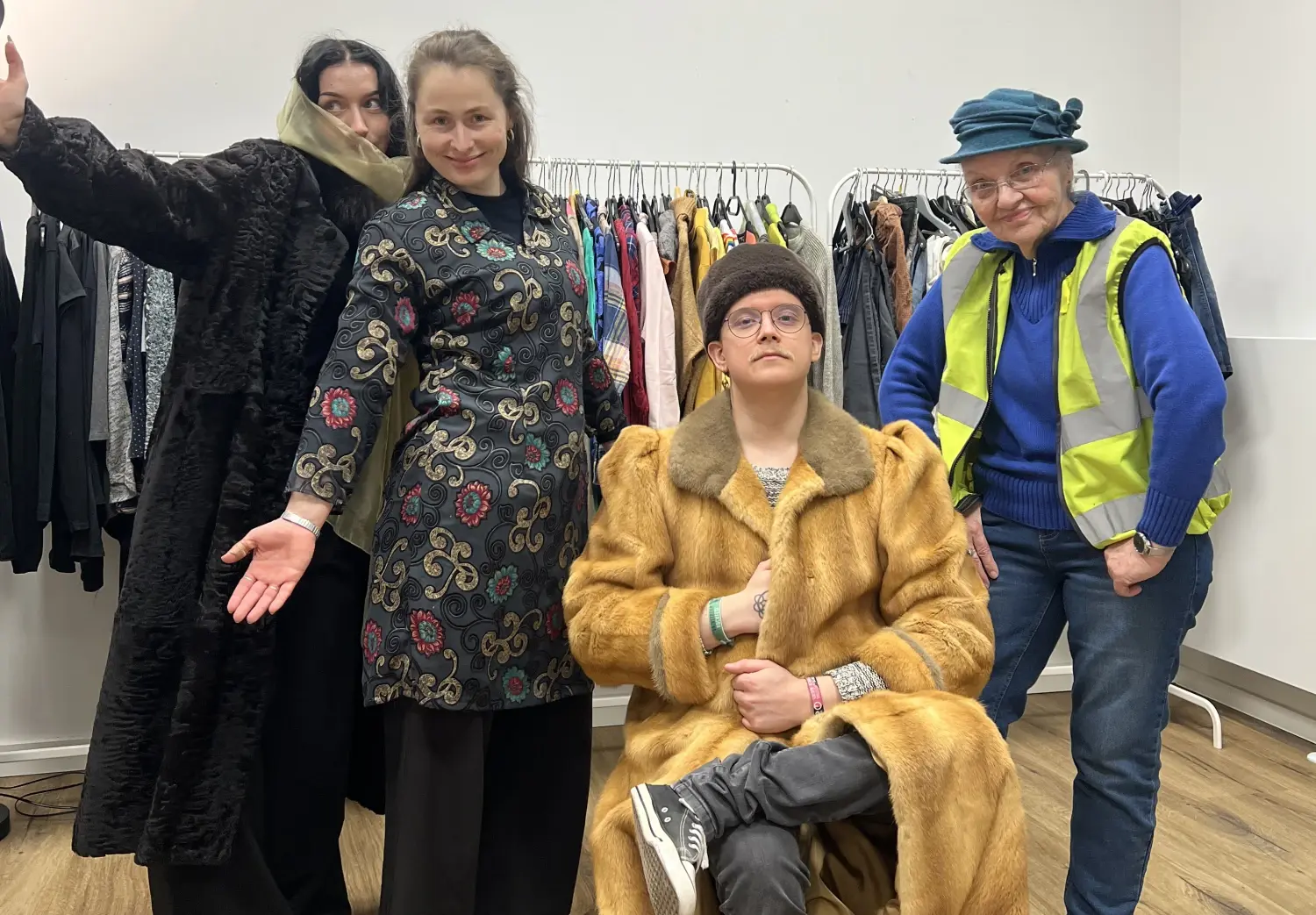 vier Personen posieren in ausgefallener Kleidung für die Kamera. Im hintergrund ist ein Kleiderständer mit vielen Klamotten.