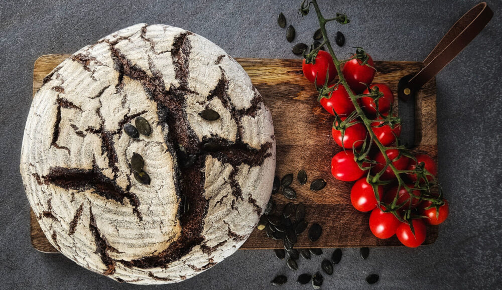 Auf einem Holzbrettchen liegt ein runder Laib Brot und Cherry-Strauchtomaten