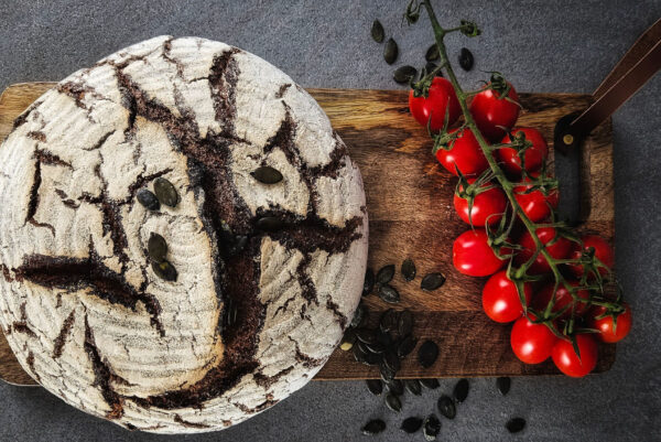 Auf einem Holzbrettchen liegt ein runder Laib Brot und Cherry-Strauchtomaten