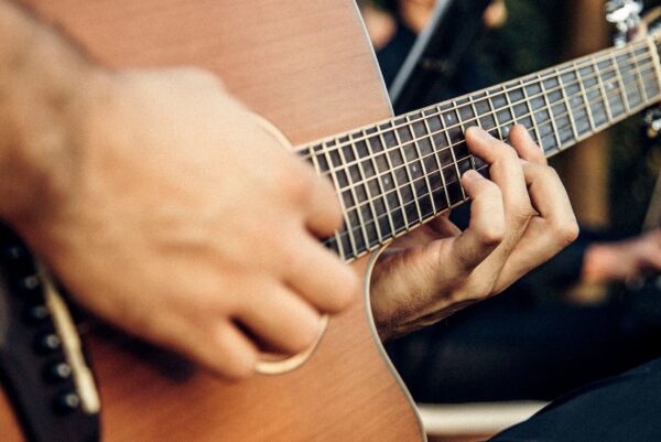 Eine akustische Gitarre in Großaufnahme wird von einer Person gehalten, die nur mit ihren Händen zu sehen ist.