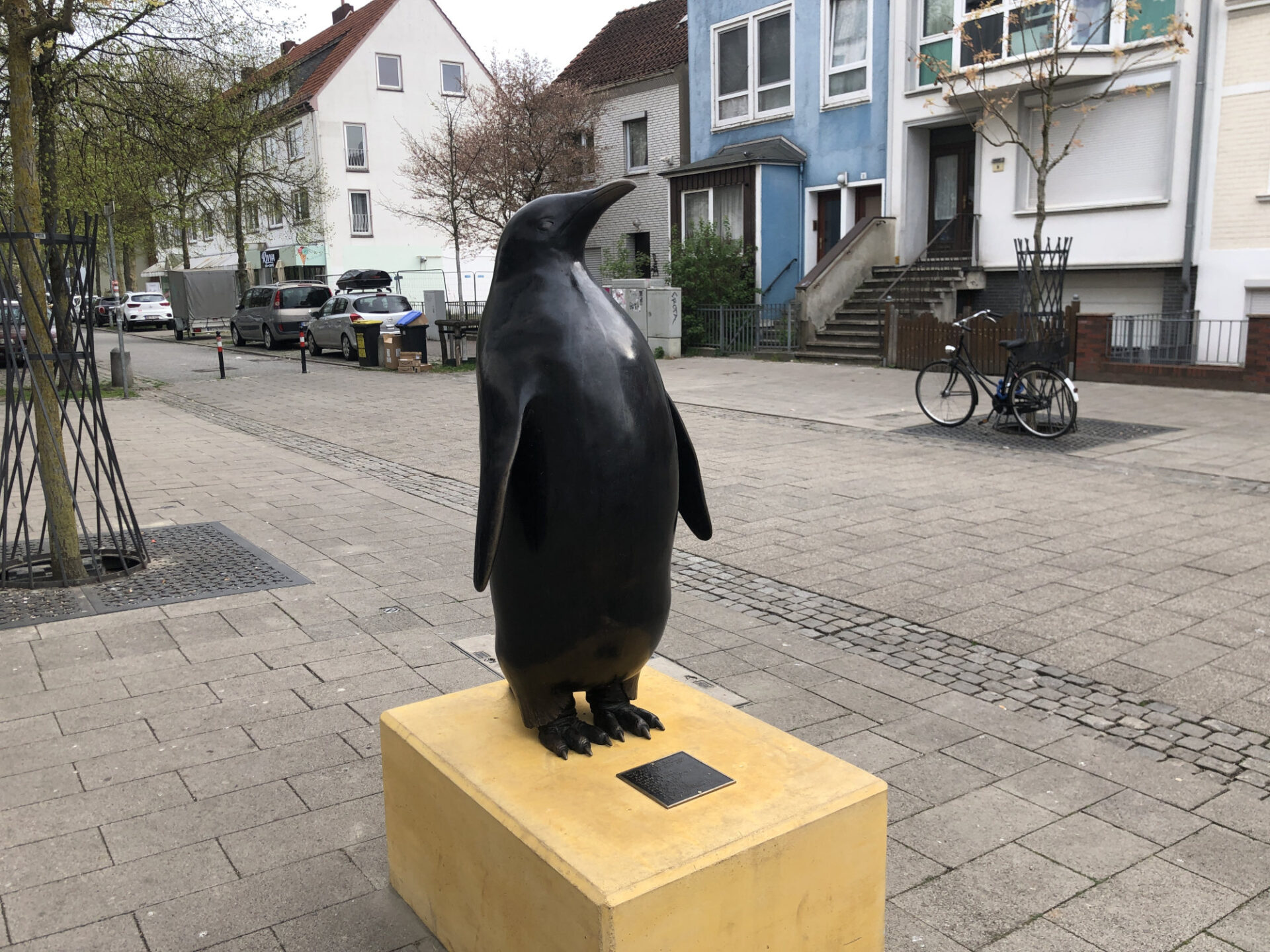 Eine Bronzeskulptur in Form eines Pinguins steht auf einem gelben Betonsockel. 