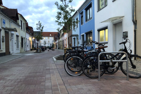Zu sehen ist die Gestaltung der Rasteder Straße in Bremen Gröpelingen nach der Klimaangepassten Sanierung: ein lockeres Plaster, neue Bäume, Fahrradparkplatze und Parkbuchten sind zu sehen.