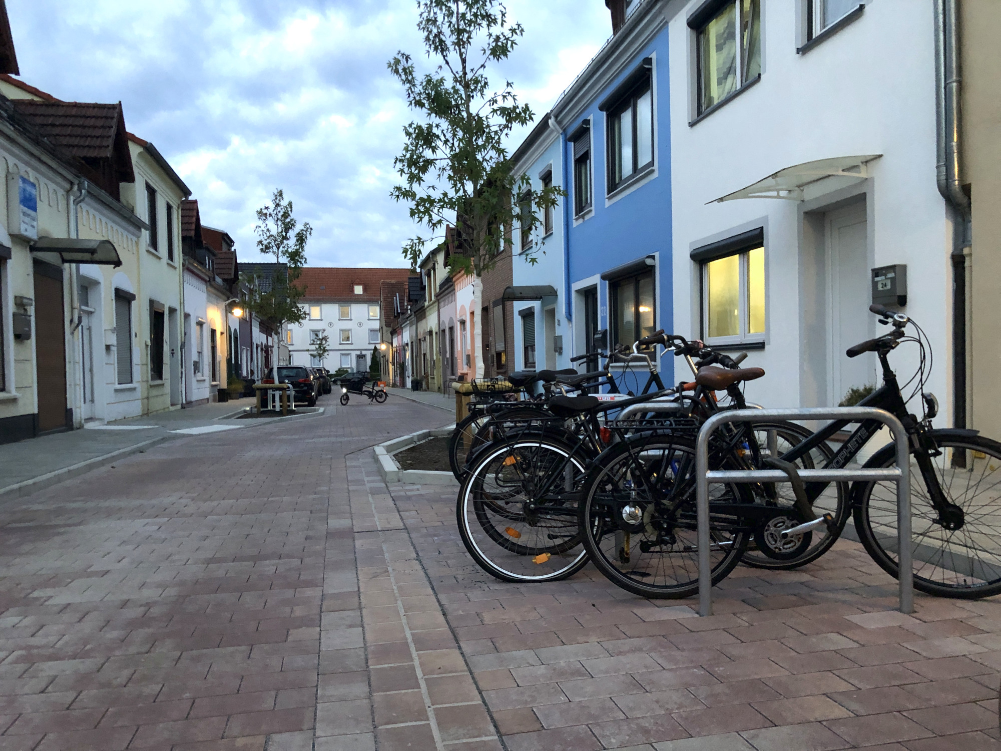 Zu sehen ist die Gestaltung der Rasteder Straße in Bremen Gröpelingen nach der Klimaangepassten Sanierung: ein lockeres Plaster, neue Bäume, Fahrradparkplatze und Parkbuchten sind zu sehen.