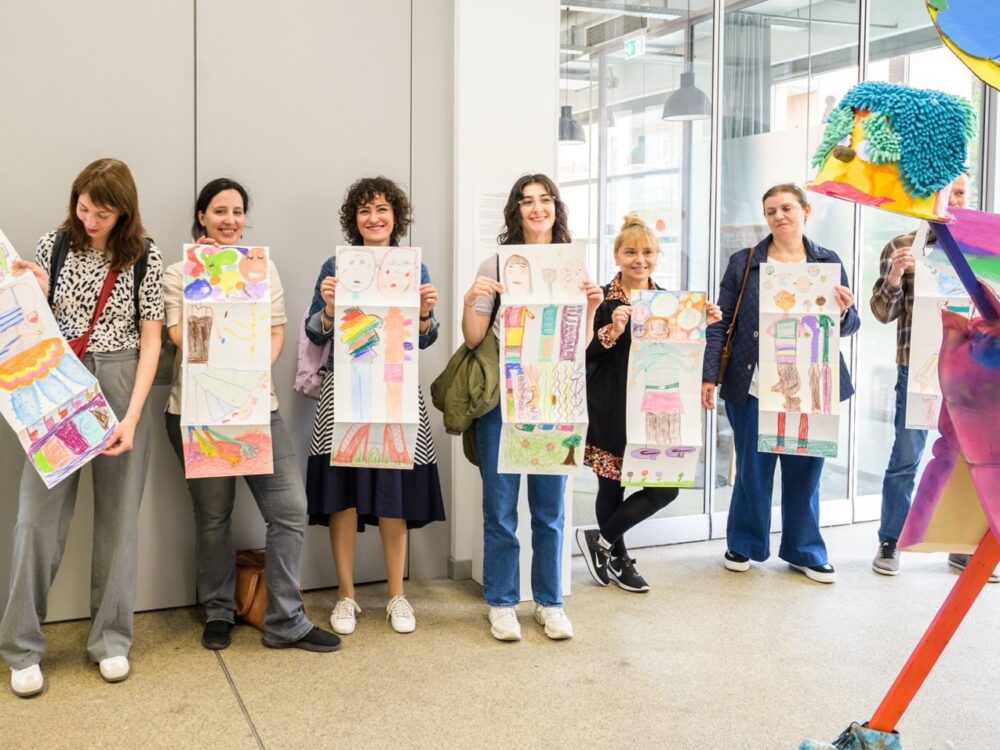 Sieben Personen halten Plakate in der Hand mit Zeichnungen darauf.
